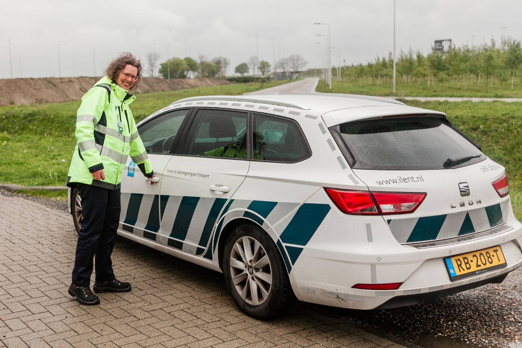 Portret van Janny bij haar auto. Zij is inspecteur vervoer gevaarlijke stoffen via de lucht bij de ILT