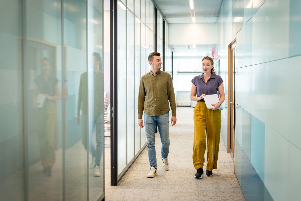 2 jonge collega's bij de ILT, pratend, lopend door de gang