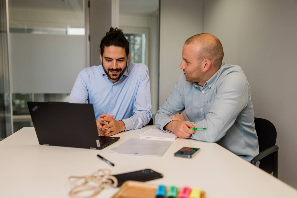 Robrecht met collega Lucas in gesprek achter de laptop. Ze werken bij de Inspectie Overheidsinformatie en Erfgoed