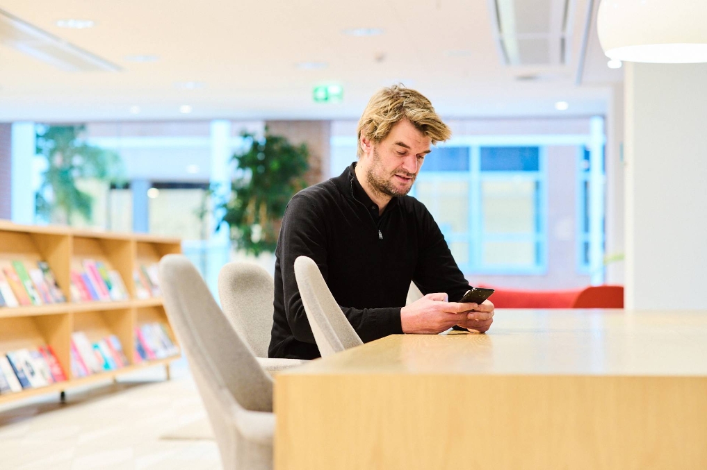 Adriaan aan een tafel bij VWS, kijkt op telefoon