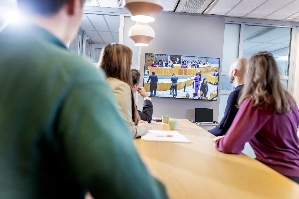Juristen bij de Rijksoverheid kijken samen naar een politiek debat in de Tweede Kamer